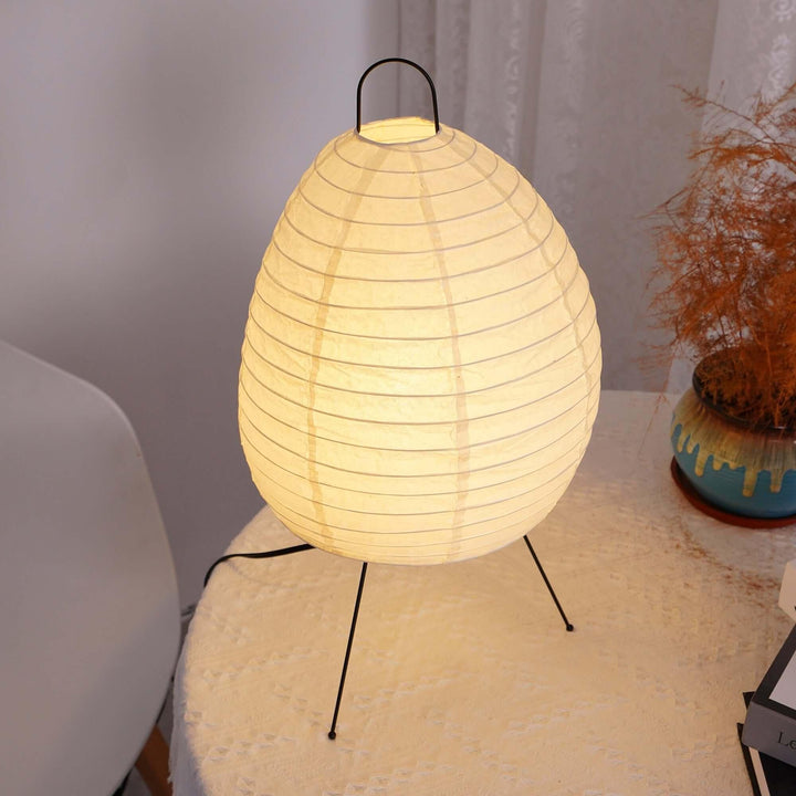 Akari 1N minimal Japandi table lamp, white, round shape, illuminating soft light on a side table, modern decor.