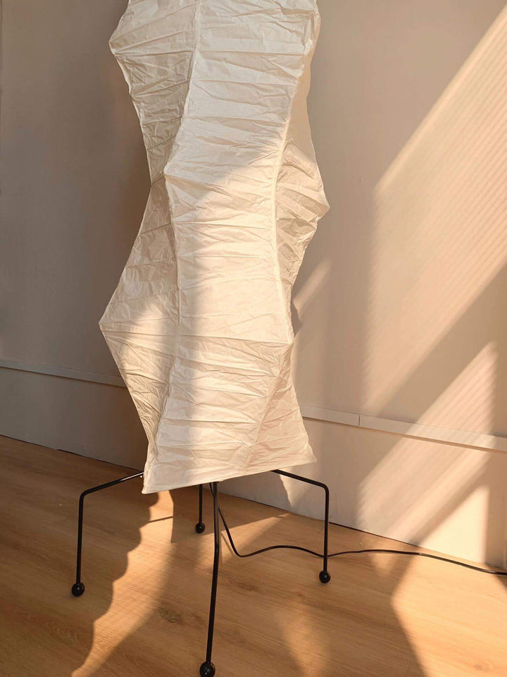 Elegant white rice paper floor lamp with minimalist design, casting soft shadows in a modern interior.
