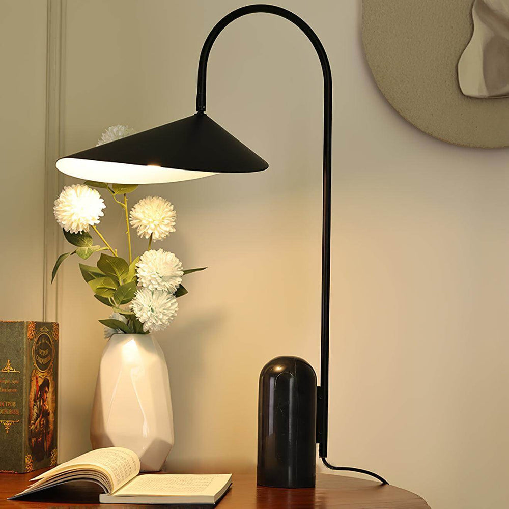 Arum table lamp in black, modern design, ideal for office or living room, alongside flowers and book on wooden table.