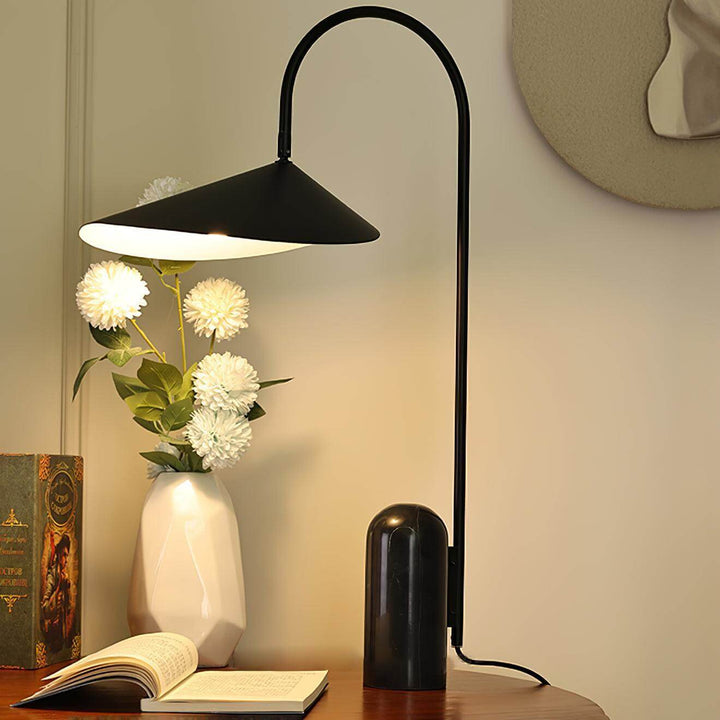 Arum table lamp in black, a modern design perfect for office and living room decor, placed beside flowers and a book.