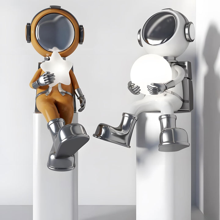 Two playful astronaut figurines, one in brown and one in white, sitting on pedestals holding glowing orbs.