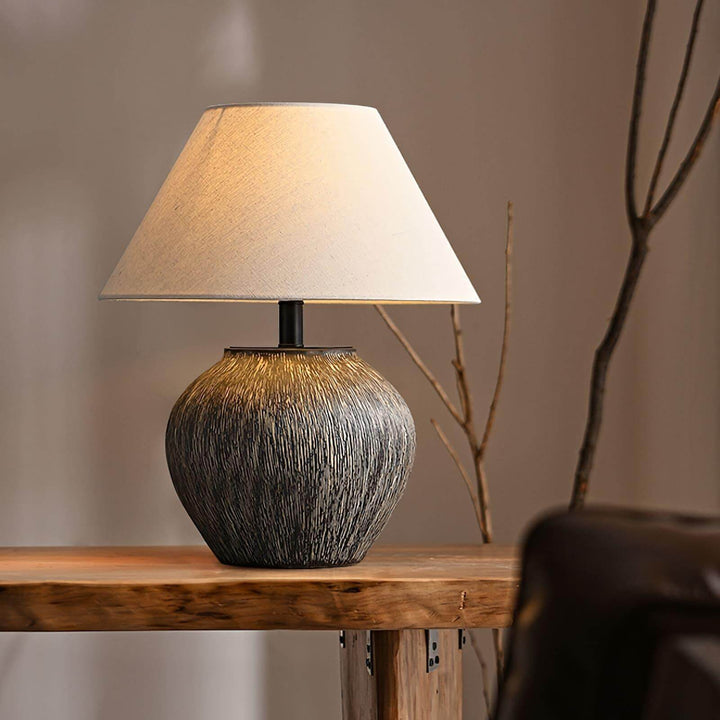 Bayi ceramic table lamp on a wooden table, featuring a textured base and a classic fabric shade, ideal for vintage decor.