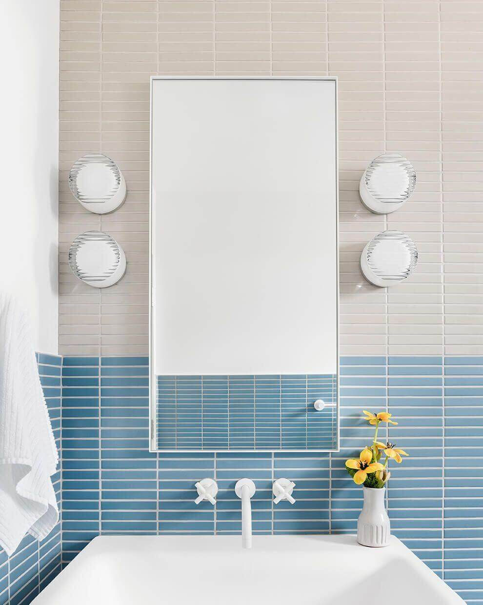 Elegant bathroom with a mirror, round vintage wall sconces, blue tile accents, and fresh flowers.