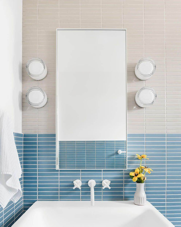 Elegant bathroom with a mirror, round vintage wall sconces, blue tile accents, and fresh flowers.
