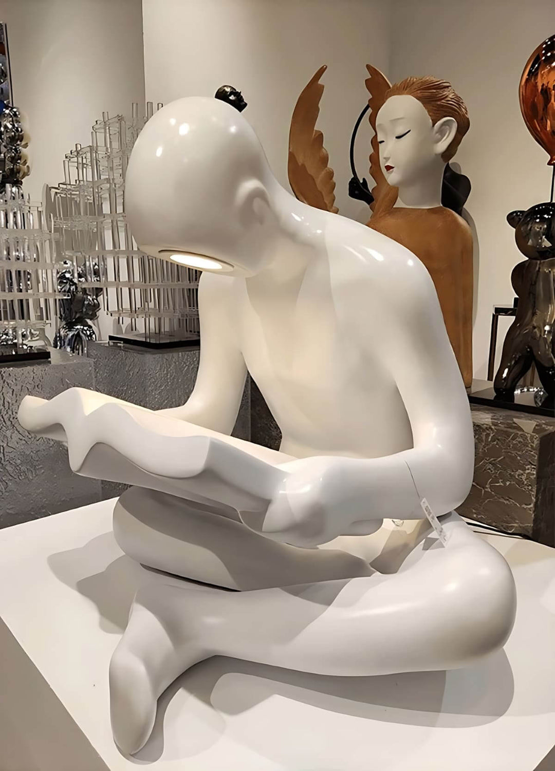 Sculptural floor lamp featuring a seated white figure reading, representing modern art decor for stylish living spaces.