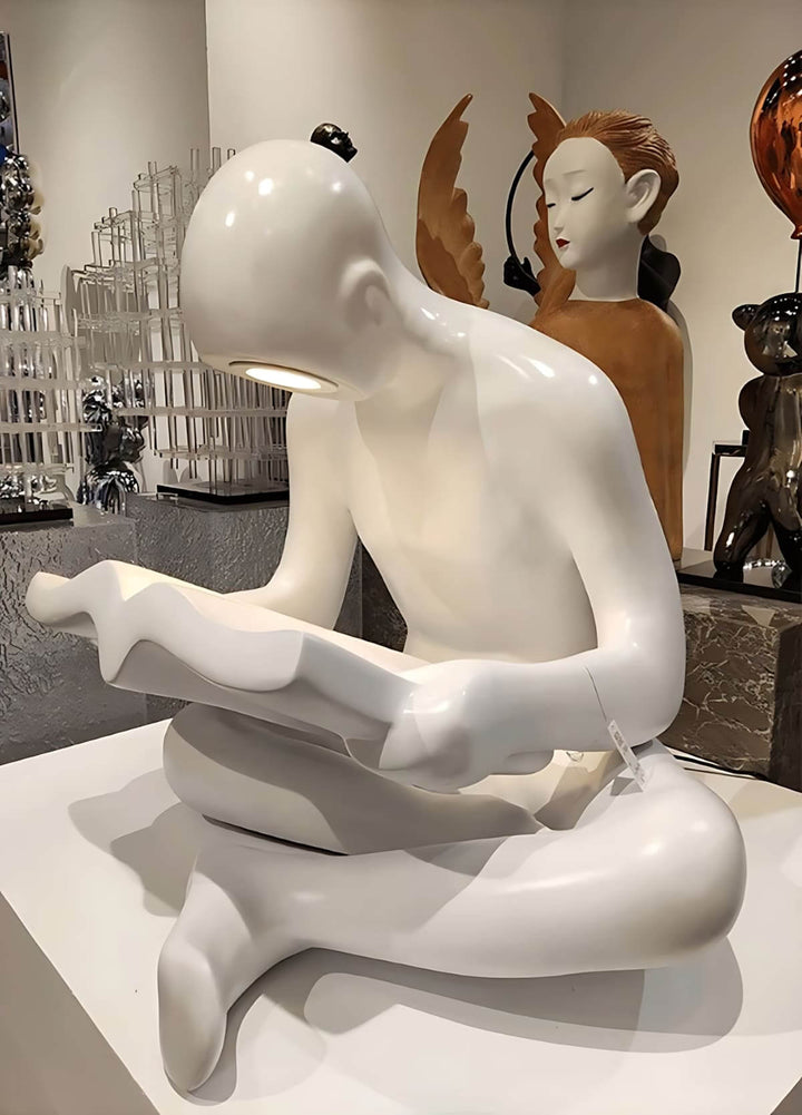 Sculptural floor lamp featuring a seated white figure reading, representing modern art decor for stylish living spaces.