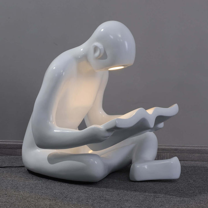 Sculptural floor lamp depicting a seated figure reading, ideal for art deco and modern living room lighting.
