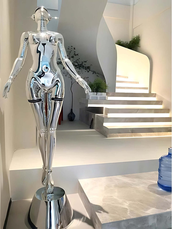 Sculptural silver mannequin with a glossy finish standing beside modern stairs in an artistic interior space.