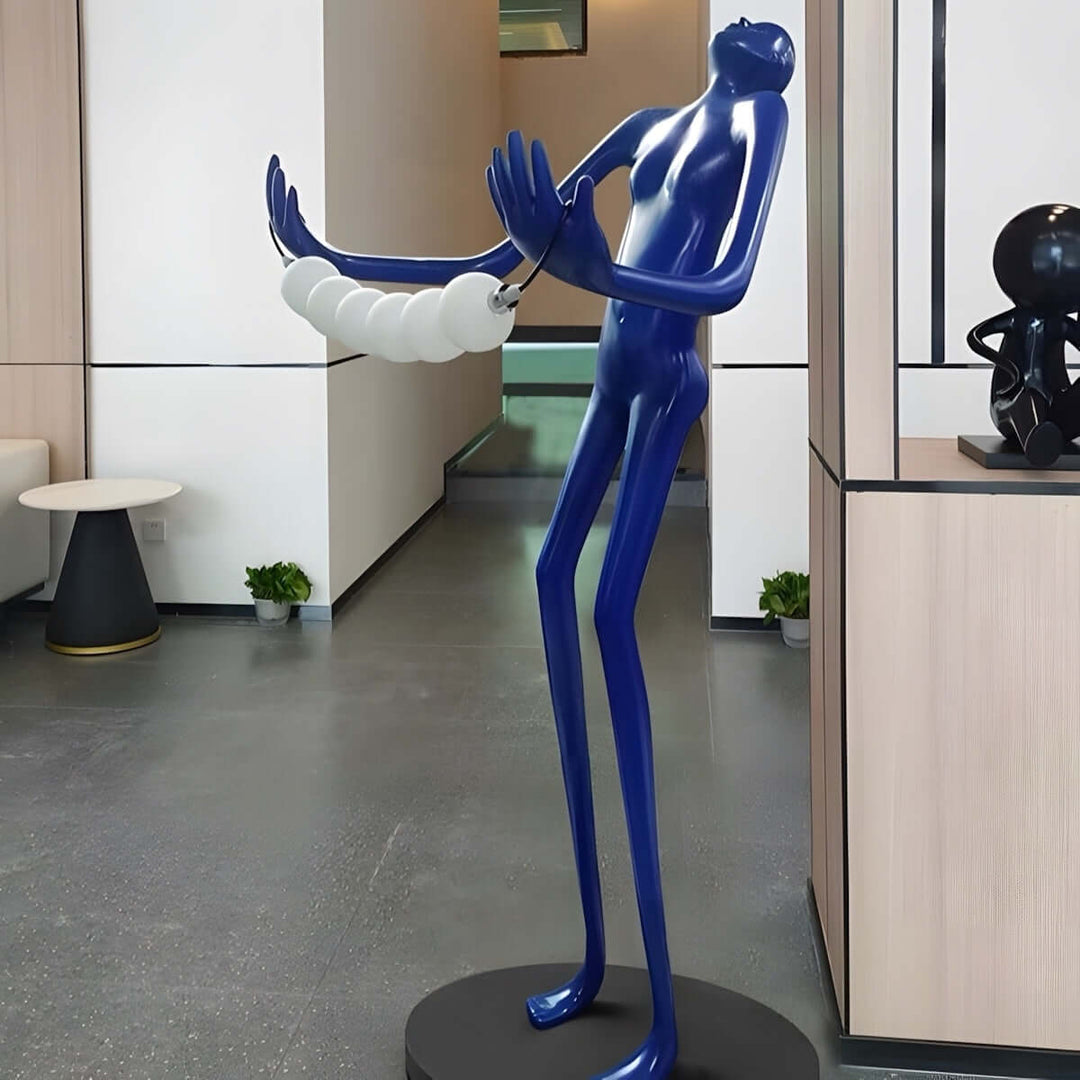 Sculptural floor lamp in art deco style, blue figure holding decorative light orbs in a modern living room setting.