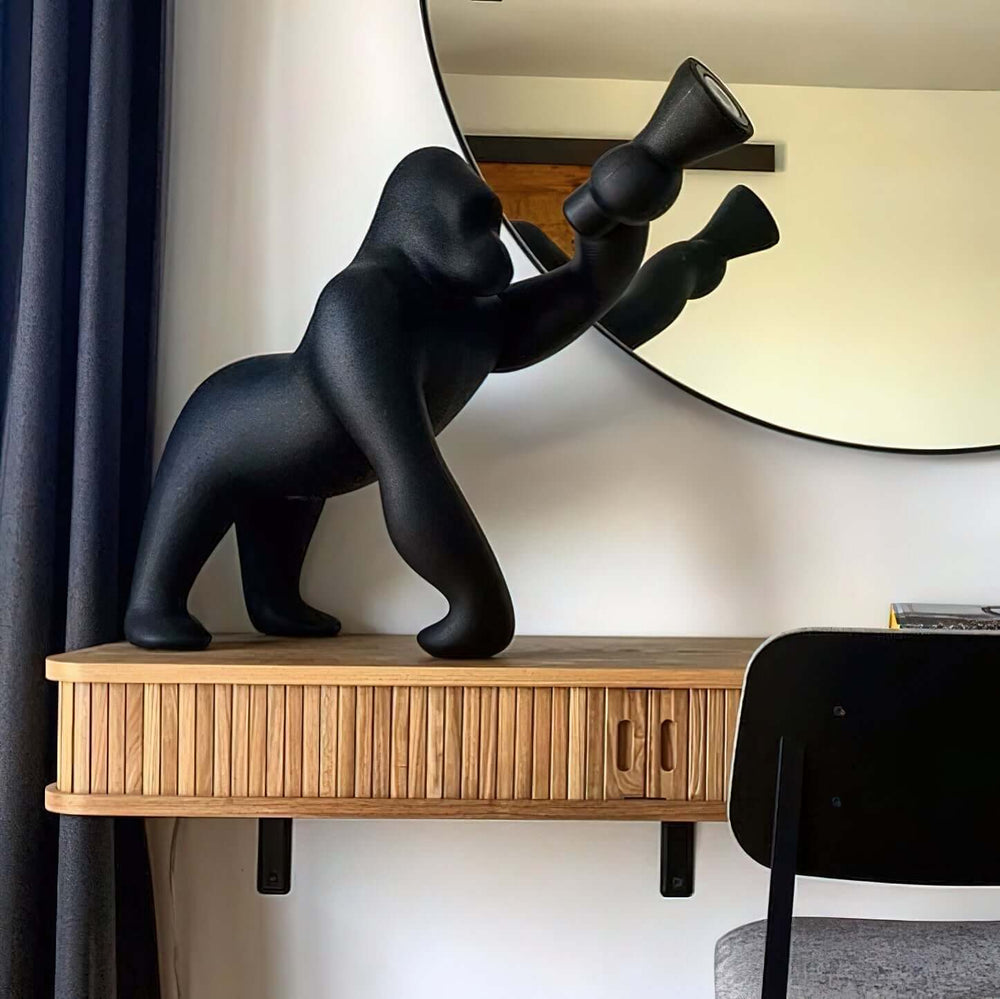 Kong sculpture floor lamp in black, showcasing a unique design on a wooden console table, with a round mirror in the background.