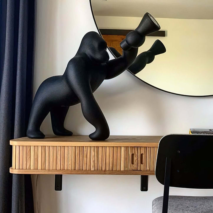 Kong sculpture floor lamp in black, showcasing a unique design on a wooden console table, with a round mirror in the background.