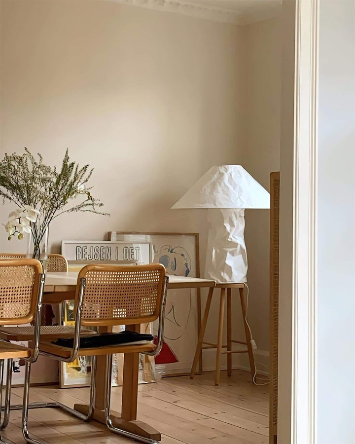 Minimal white table lamp in a bright room, showcasing modern decor with wooden dining chairs and artwork.