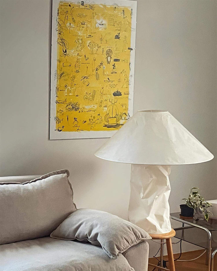 Minimal table lamp with a white shade next to a gray sofa and yellow wall art, perfect for a bedroom or living room.