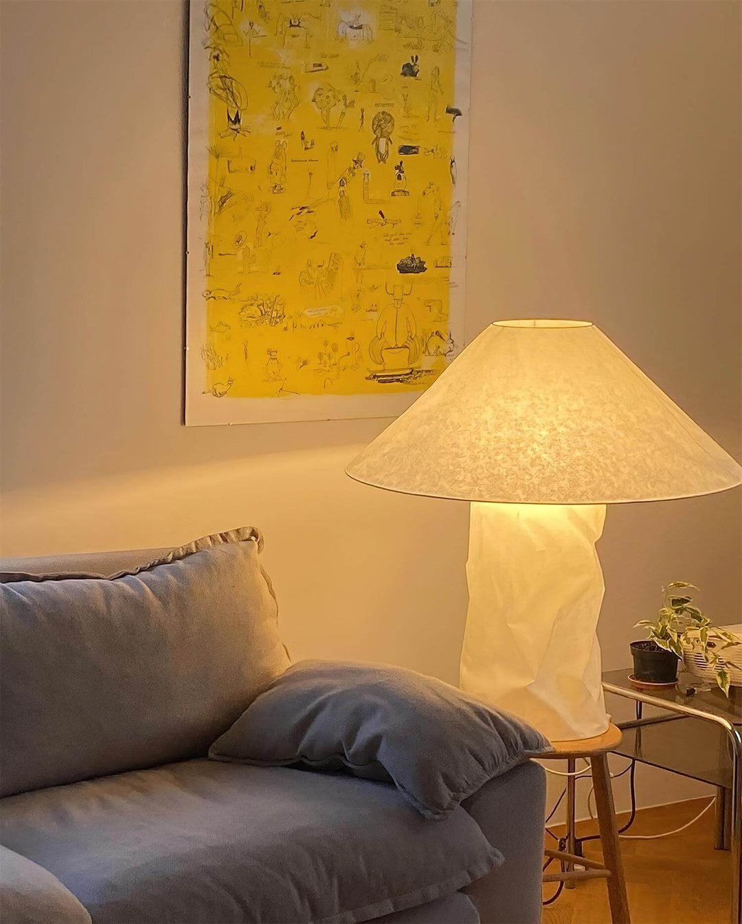 Minimal table lamp with a white shade illuminating a cozy living room with a blue sofa and abstract yellow artwork.