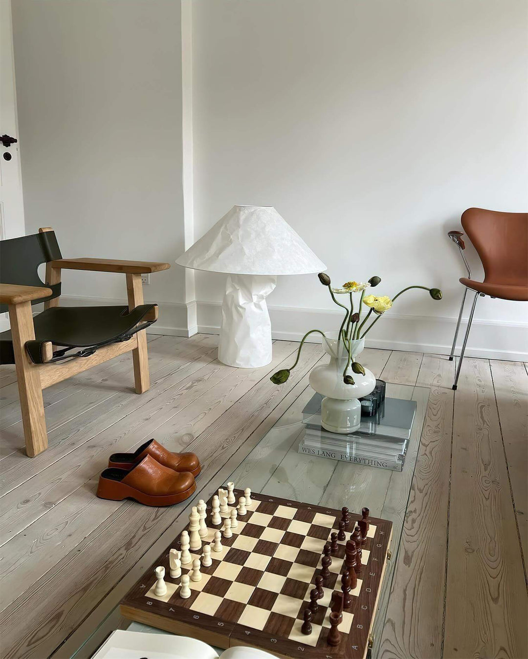 A minimalist white table lamp with a unique design, placed next to a chessboard in a stylish living room setup.