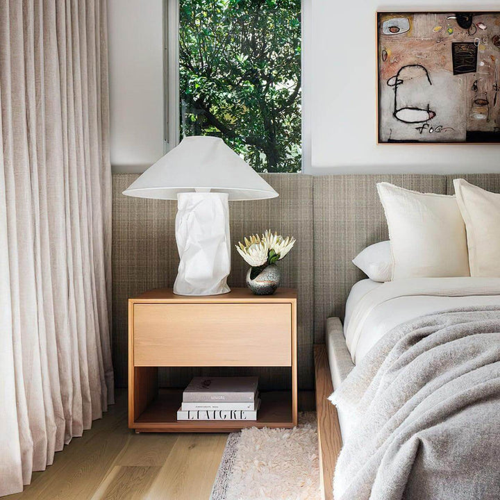 Minimal table lamp in white on a bedside table, complementing a cozy bedroom with soft bedding and natural light.