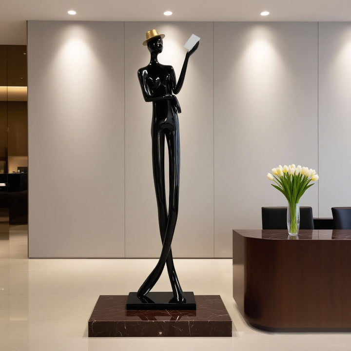 Sculptural floor lamp in art deco style featuring a tall, slender figure holding a book, perfect for living room decor.