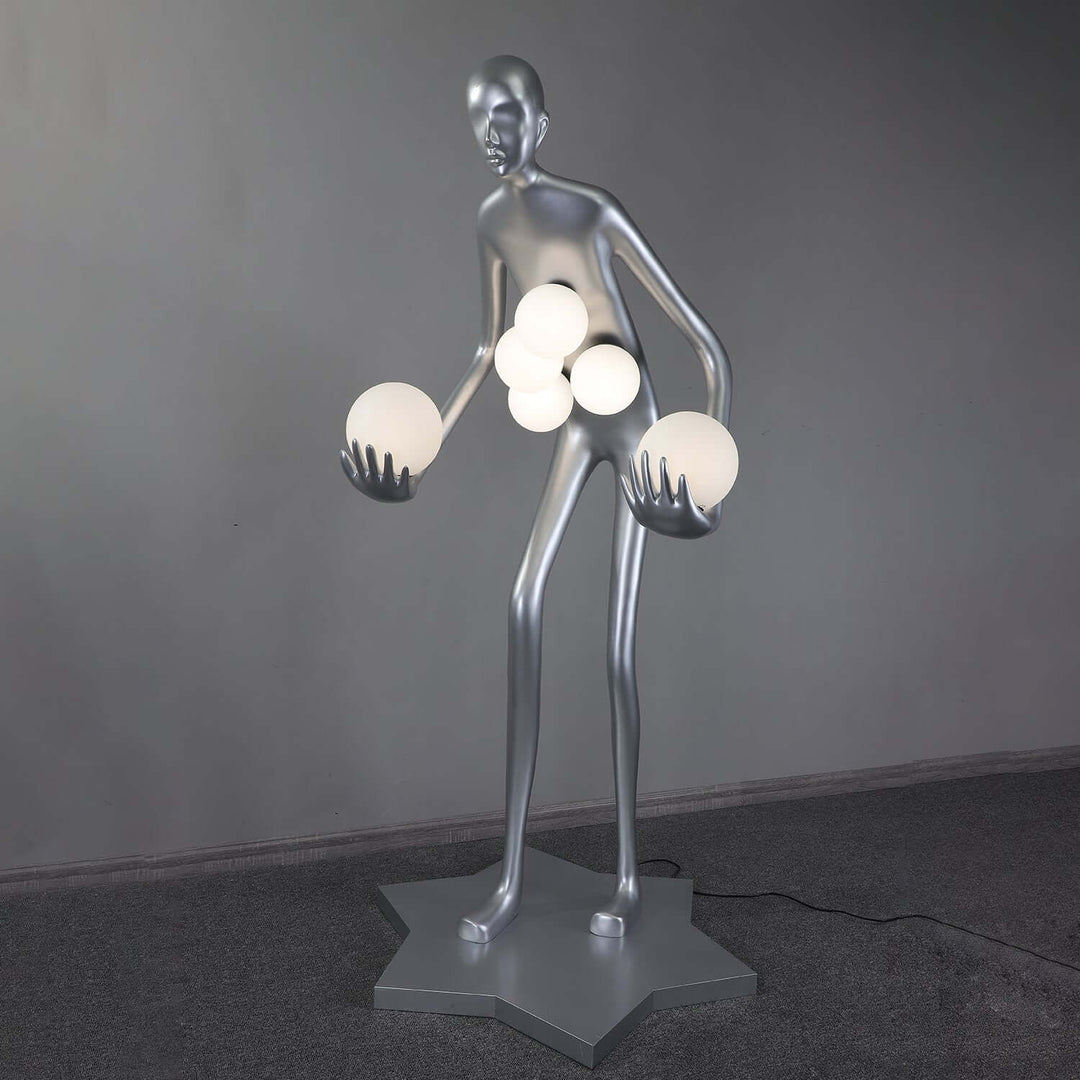 Sculptural floor lamp resembling a human figure, holding glowing orbs, perfect for modern art deco living room lighting.