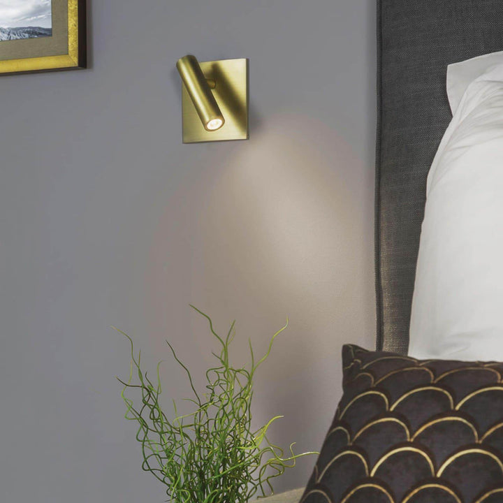 Minimalist brass flush mount wall sconce beside a bed, perfect for reading and adding style to any bedroom.