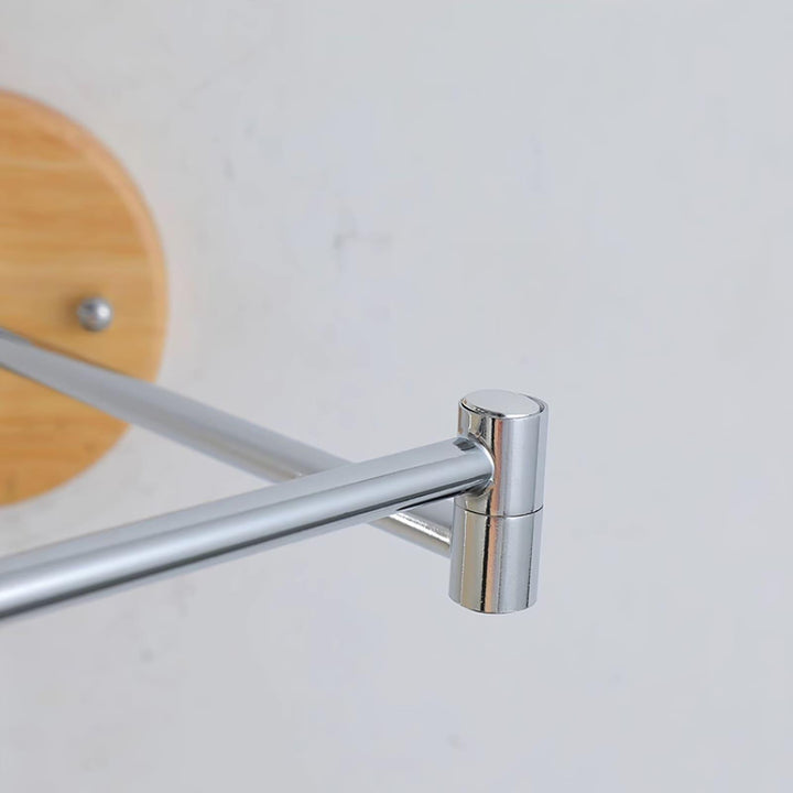 Close-up of a chrome articulating arm on a modern wall sconce, showcasing sleek design details against a wooden mount.