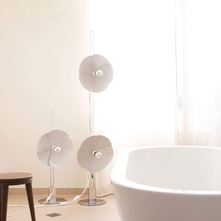 Modern white floor lamps with flower design beside a bathtub in a bright, airy bathroom.