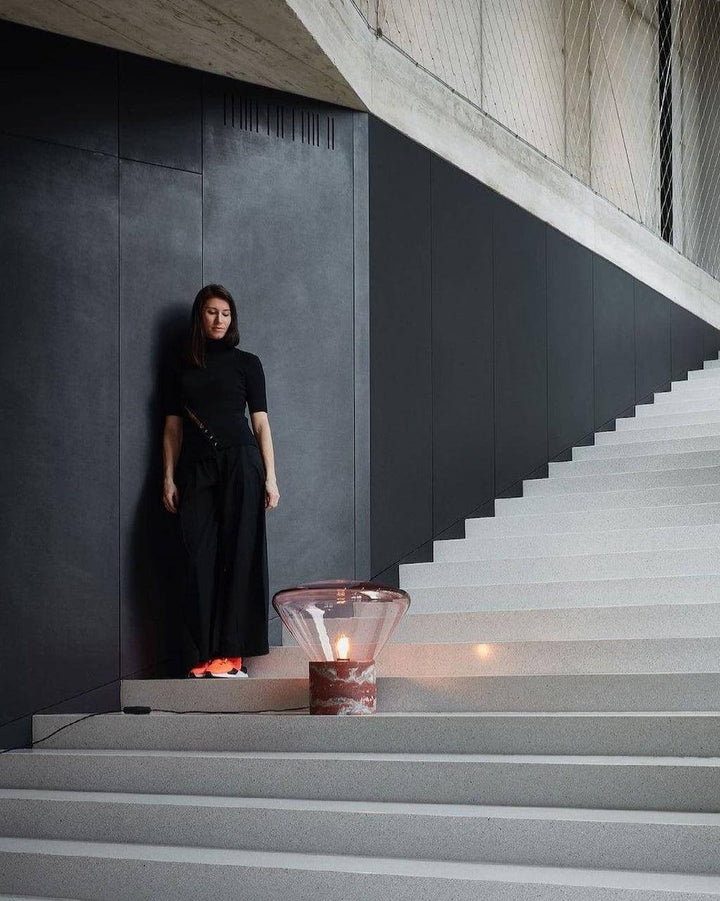 Elegant woman in black outfit beside a stylish round glass table lamp on minimalist stairs, showcasing modern lighting design.