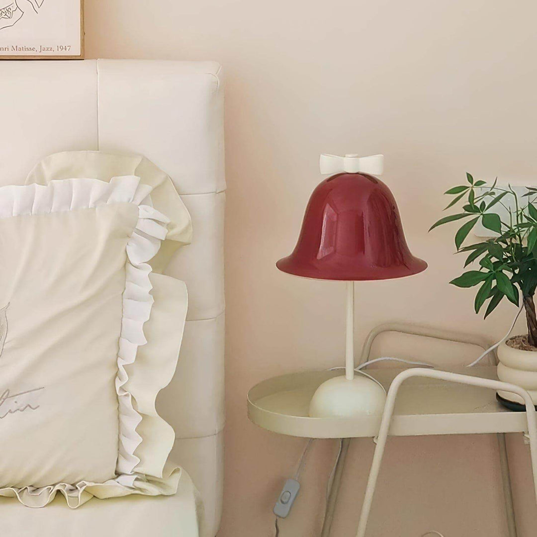 Cute red bell-shaped lamp with a bow on a bedside table, perfect for a cozy bedroom or dining room.