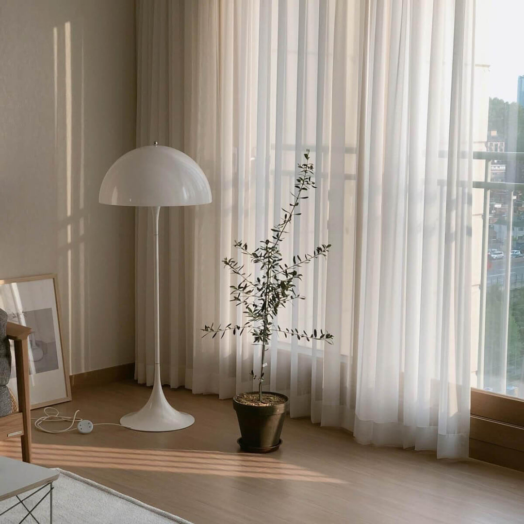 Modern white acrylic floor lamp in bright living room beside a potted plant, creating an elegant atmosphere.