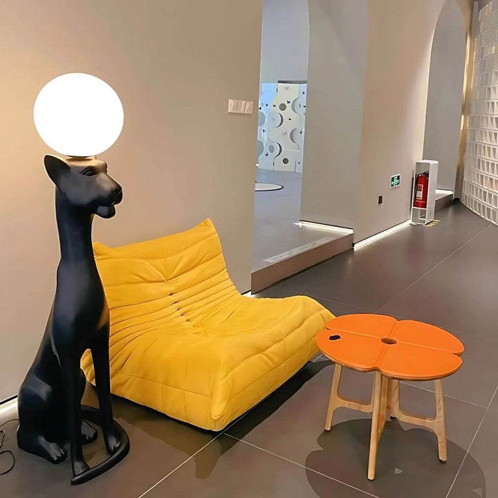 Sculptural floor lamp beside a yellow lounge chair and a round orange table in a modern living space.