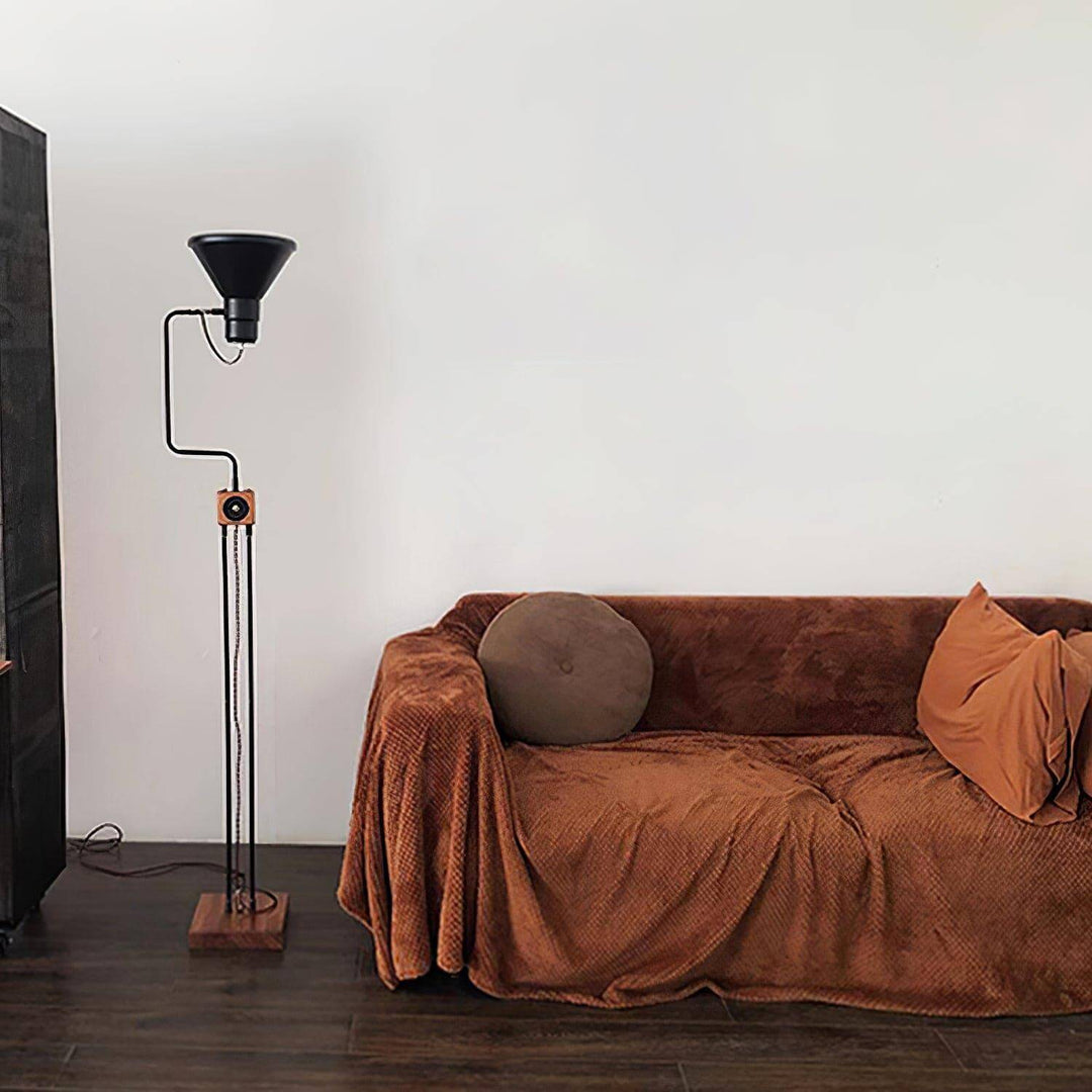 Retro Toia industrial floor lamp in black standing next to a cozy brown sofa, perfect for a stylish corner.
