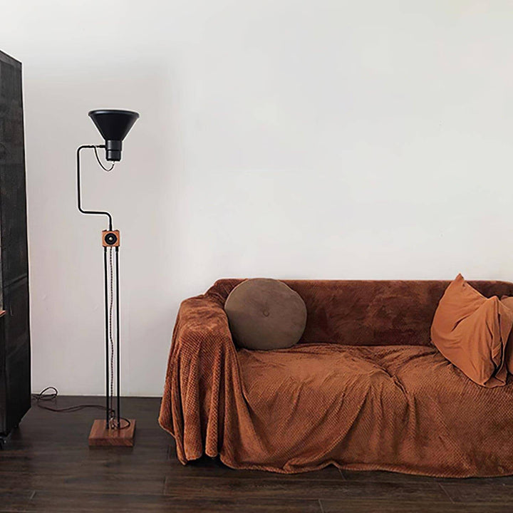 Retro Toia industrial floor lamp in black standing next to a cozy brown sofa, perfect for a stylish corner.