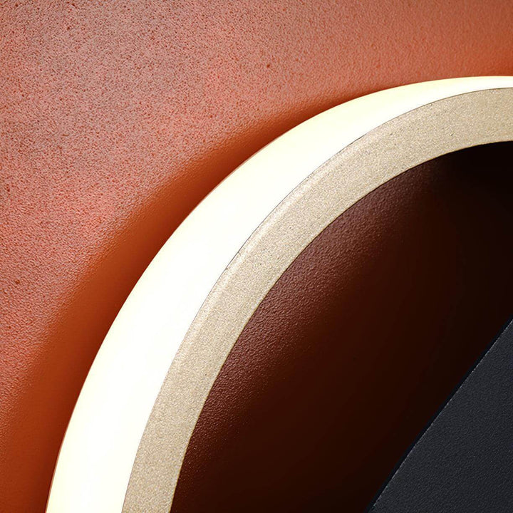Close-up of a contemporary wall light with a sleek design, highlighting its curved edge and warm glow against an orange wall.