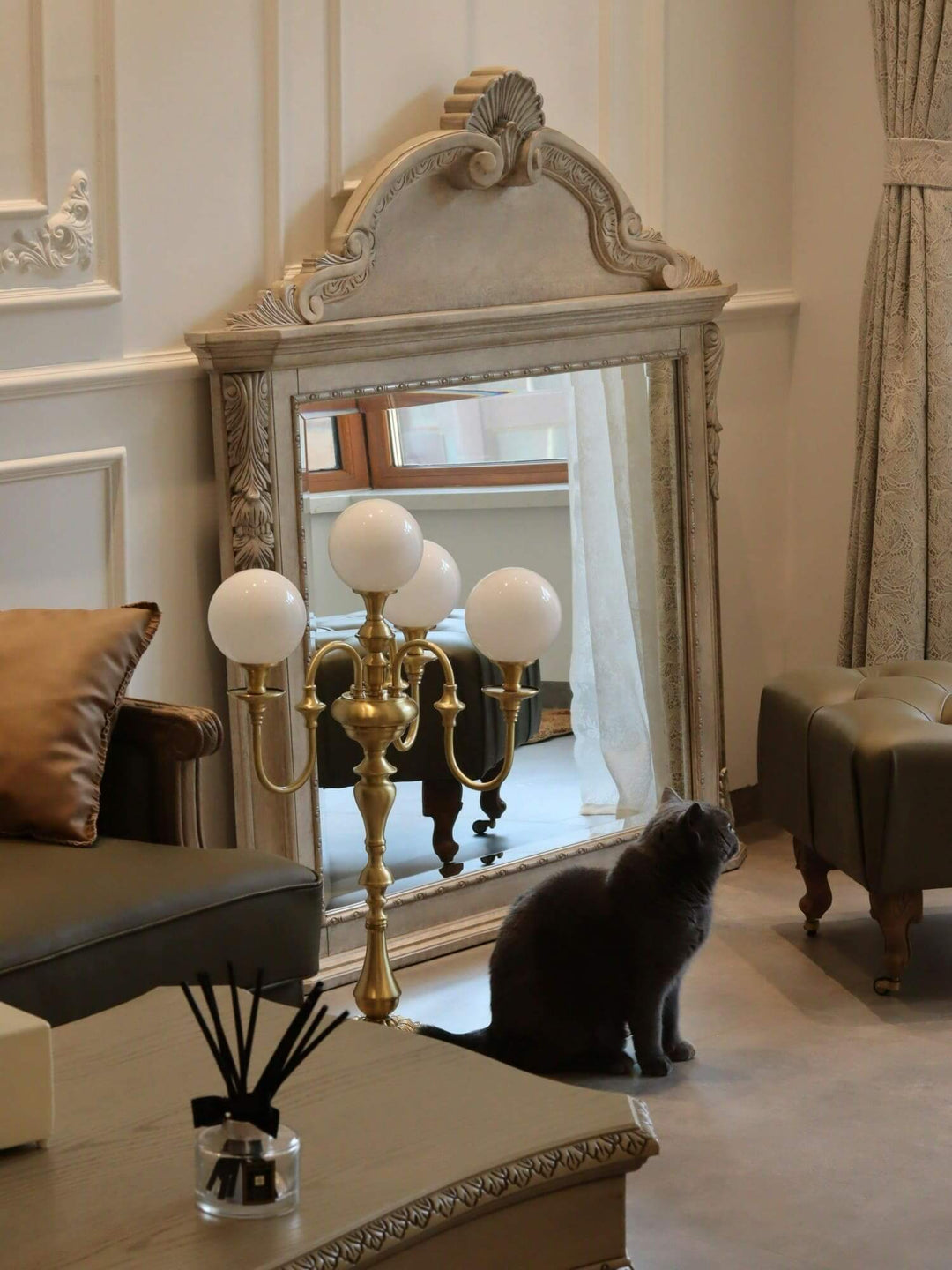 Brass table light next to a sofa and a large mirror, with a cat sitting nearby in a stylish living room setting.