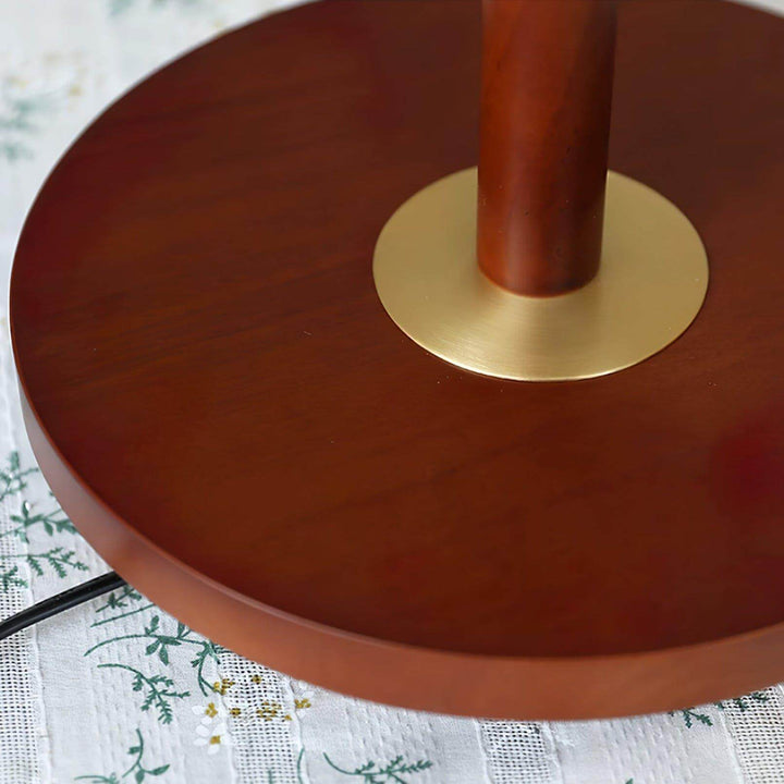 Close-up of the wooden base and brass detail of a mid century modern floor lamp on a patterned tablecloth.