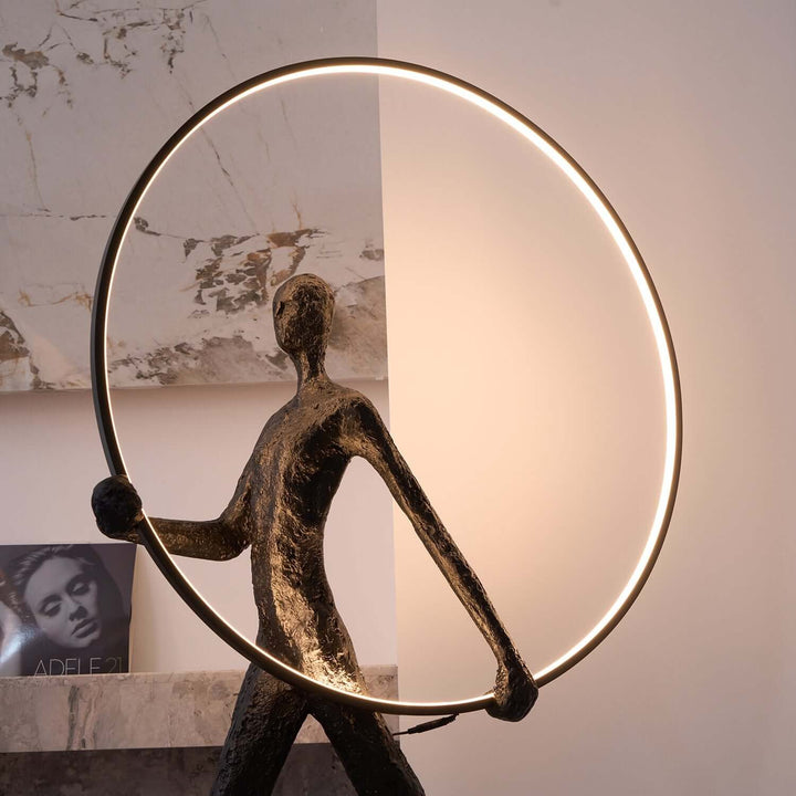 Sculptural floor lamp with a figure holding a circular light, perfect for modern art deco living room decor.