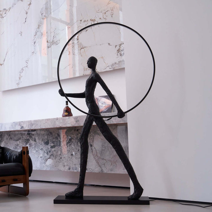 Sculptural floor lamp resembling a figure holding a hoop, ideal for art deco style living rooms.