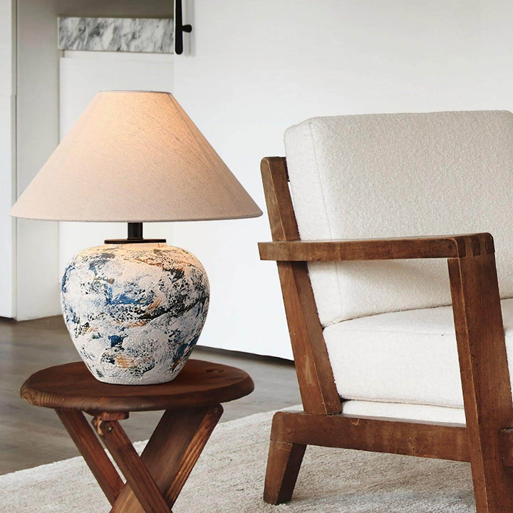 Neoclassical ceramic table lamp on a wooden side table beside a comfortable armchair in a stylish living room.