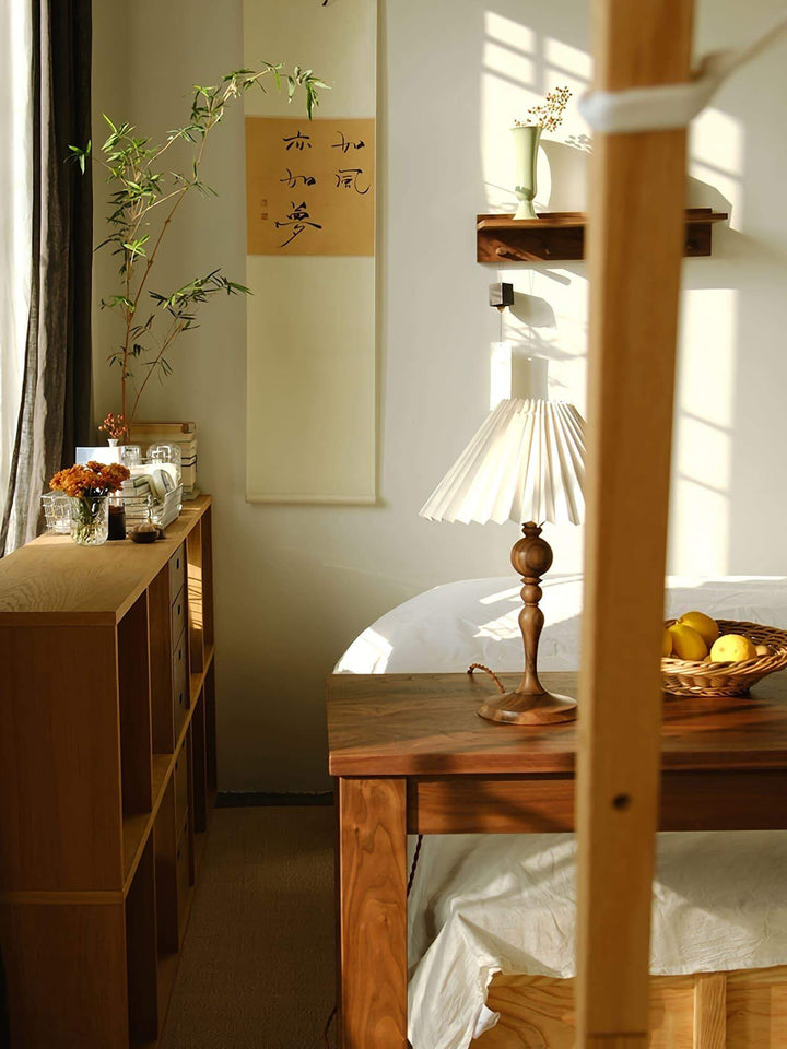 Zulu pleated table lamp on side table in a cozy room with wood furniture and warm lighting.