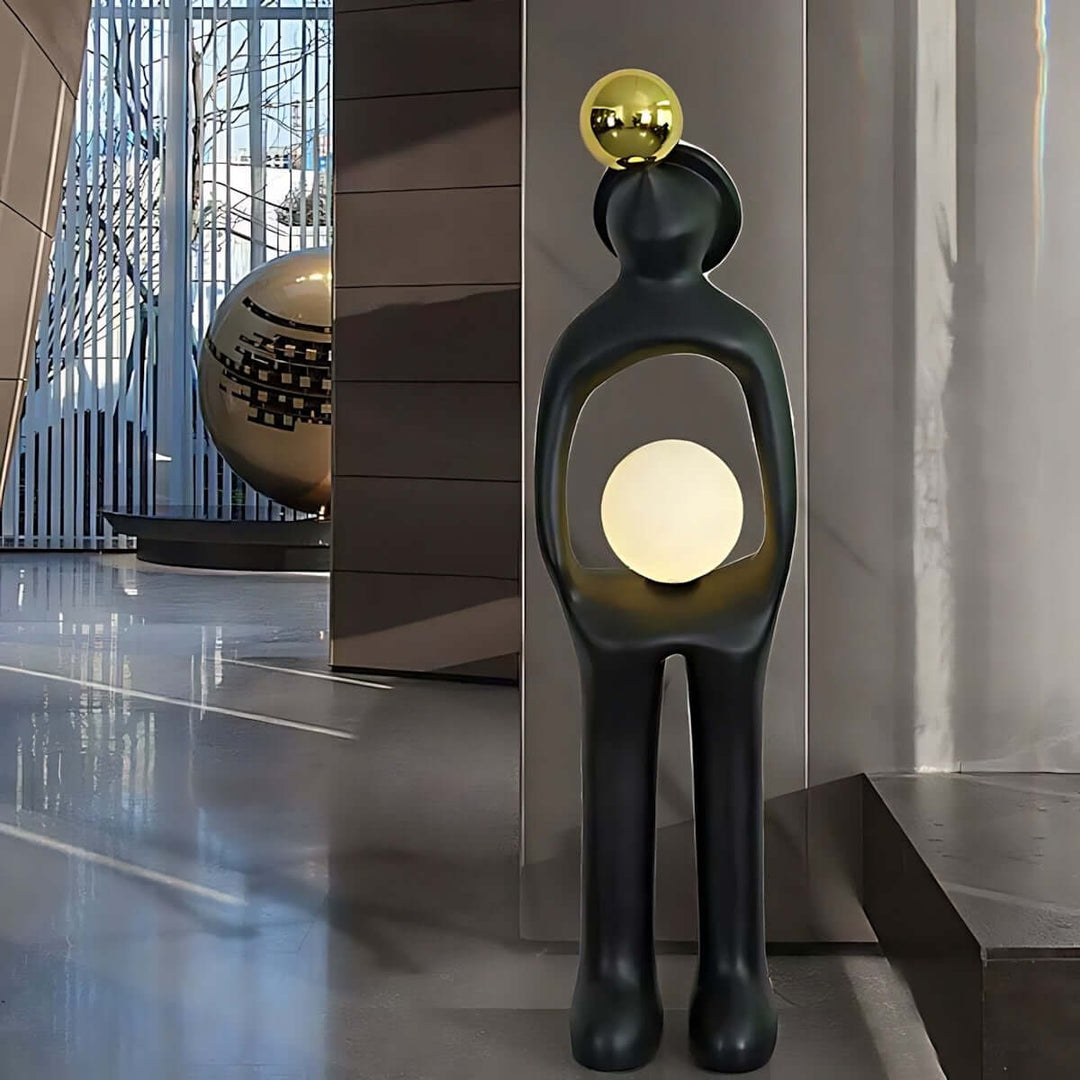 Sculptural art deco floor lamp in living room with black figure holding a glowing orb and a gold accent.