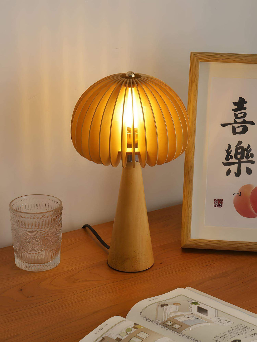 Wooden pumpkin table lamp casting warm light on a desk, paired with a glass and art print, perfect for cozy decor.