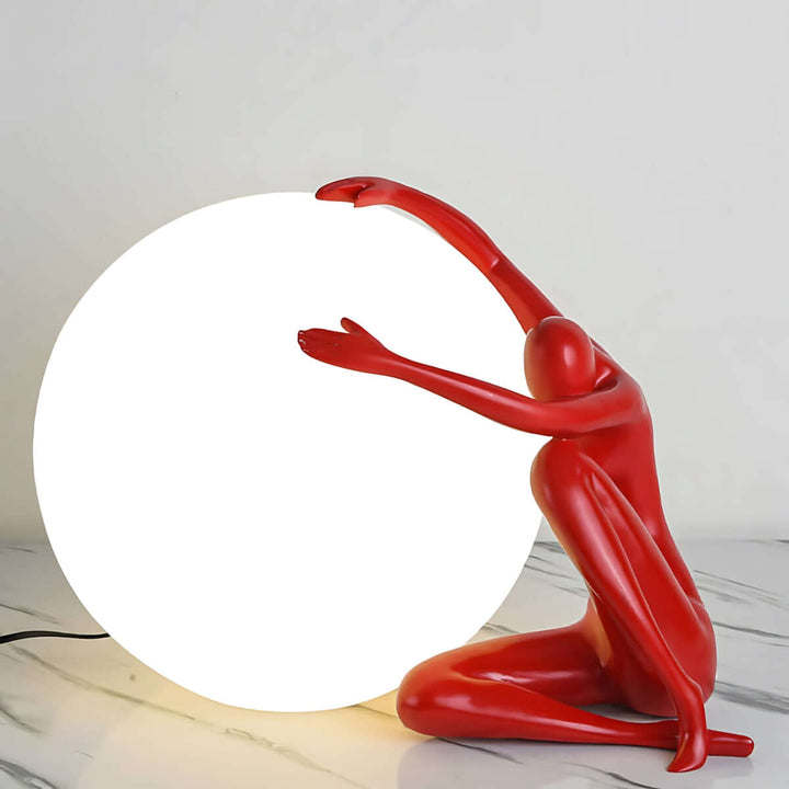 Zelvora sculptural table lamp, an art deco design featuring a red figure embracing a glowing orb, ideal for living room decor.
