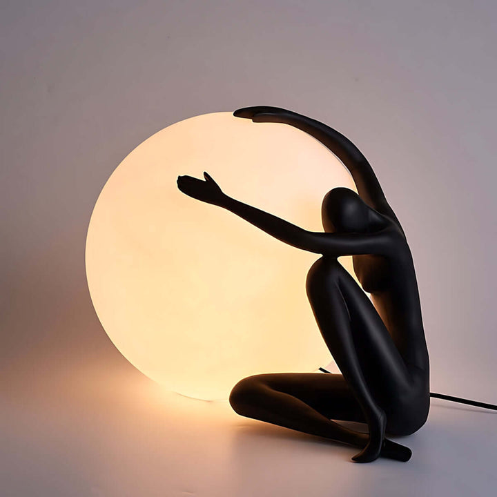 Zelvora sculptural table lamp featuring a black figure embracing an illuminated circular shade, perfect for art deco living room lighting.