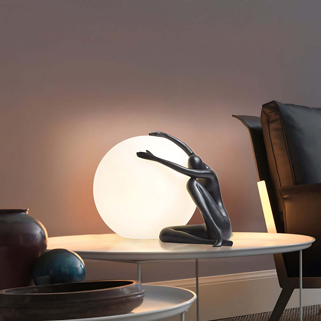 Zelvora sculptural table lamp featuring a black figure cradling a round light, ideal for art deco style living rooms.