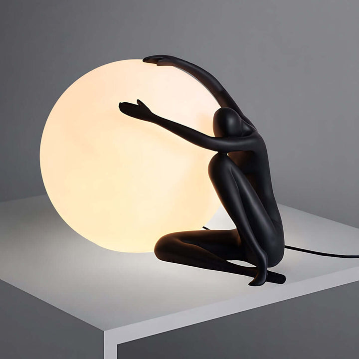 Zelvora sculptural table lamp in black, featuring a gracefully embracing figure with a glowing orb, perfect for art deco decor.