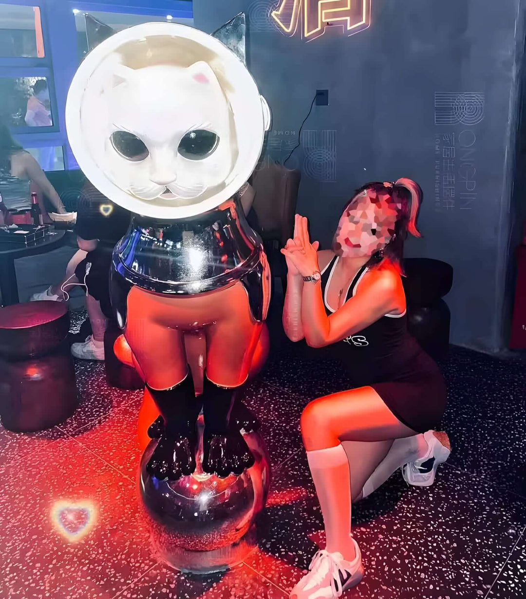 A playful scene featuring a person posing next to a whimsical cat sculpture in a vibrant setting.