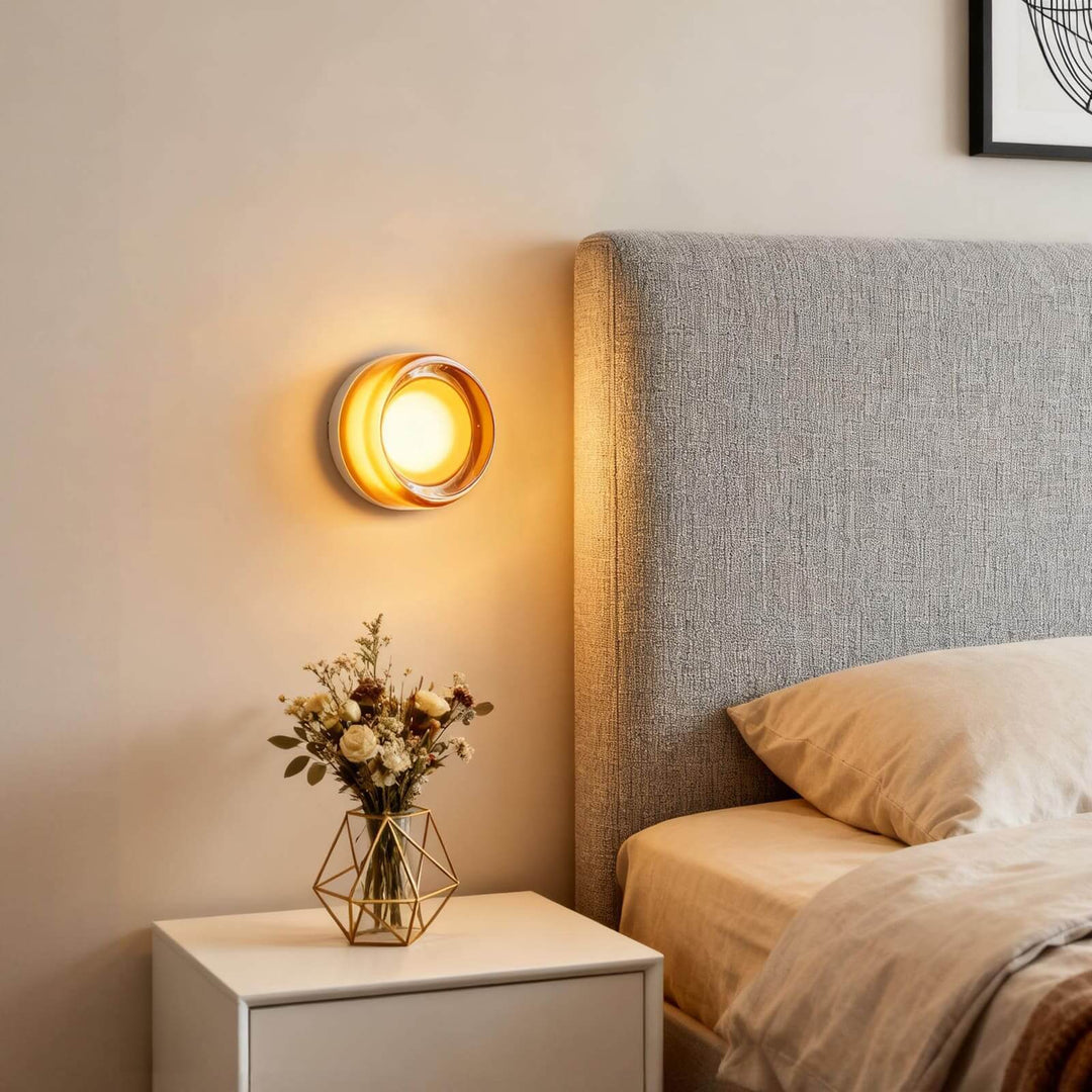 Amber glass wall sconce glowing beside a bedroom headboard and white nightstand.