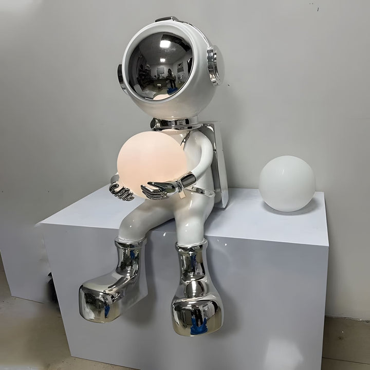 Sculptural astronaut lamp holding a glowing orb, perfect for modern decor and unique lighting.