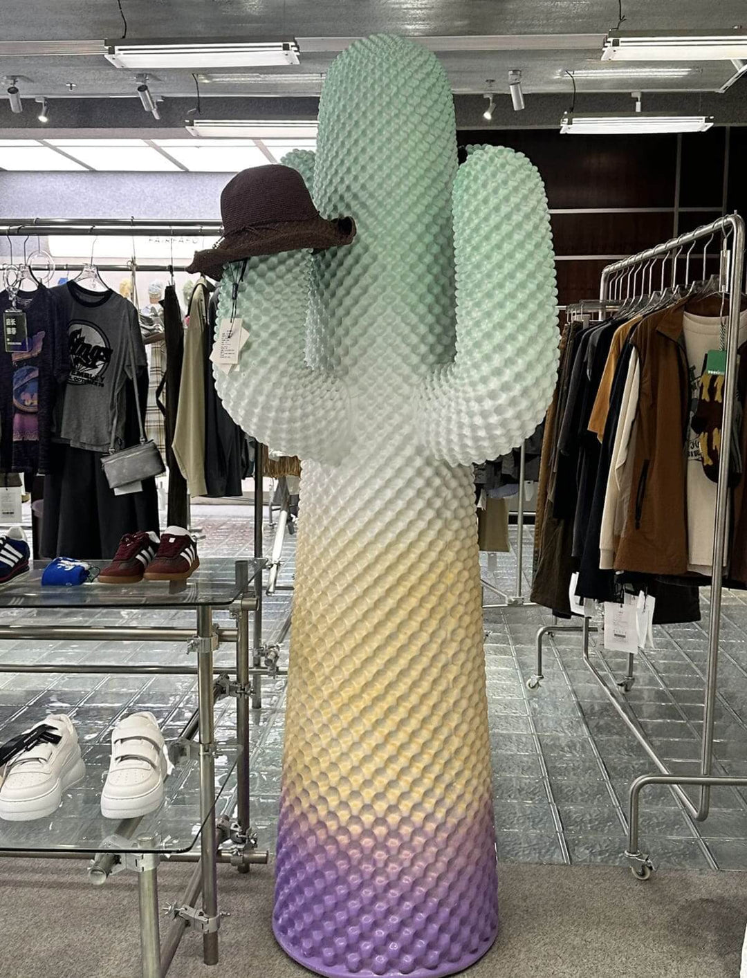 Colorful cactus sculpture wearing a hat, displayed in a trendy boutique showcasing fashion items.