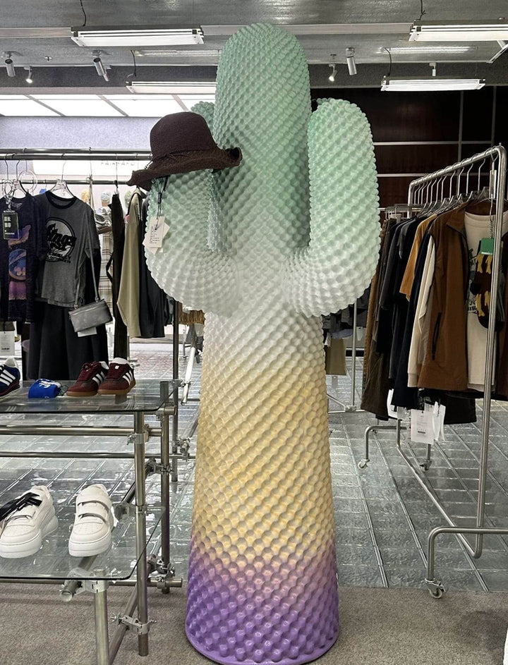 Colorful cactus sculpture wearing a hat, displayed in a trendy boutique showcasing fashion items.
