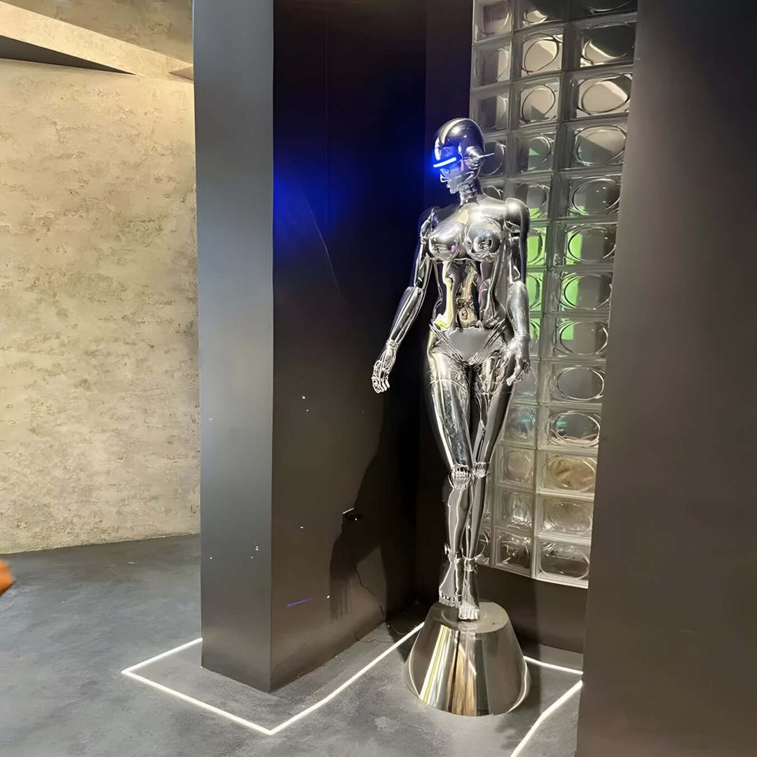 Sleek sculptural robot figure with metallic finish, standing near glass wall in modern interior space.